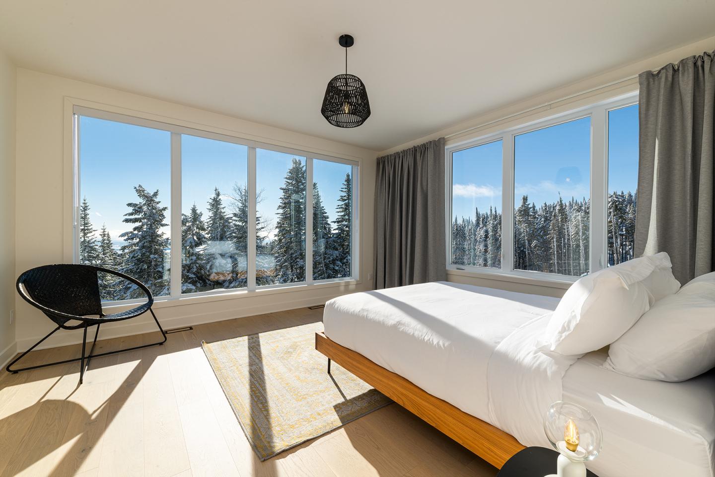 Chambre lumineuse avec lit, fauteuil noir et vue sur forêt enneigée.
