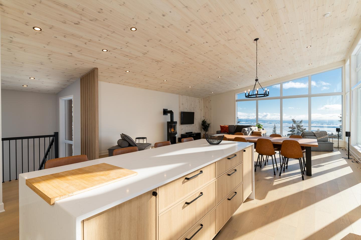 Cuisine moderne en bois, vue sur un salon et de grandes fenêtres.