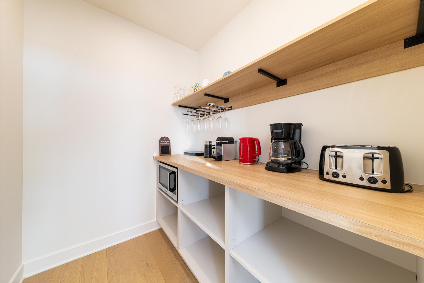 Petite cuisine avec étagères en bois, cafetière, grille-pain et bouilloire rouges.