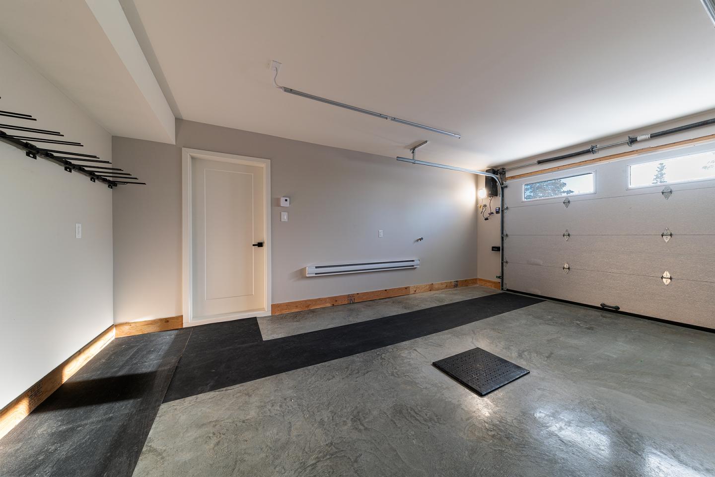Garage vide avec un sol en béton poli et une porte blanche entrouverte.