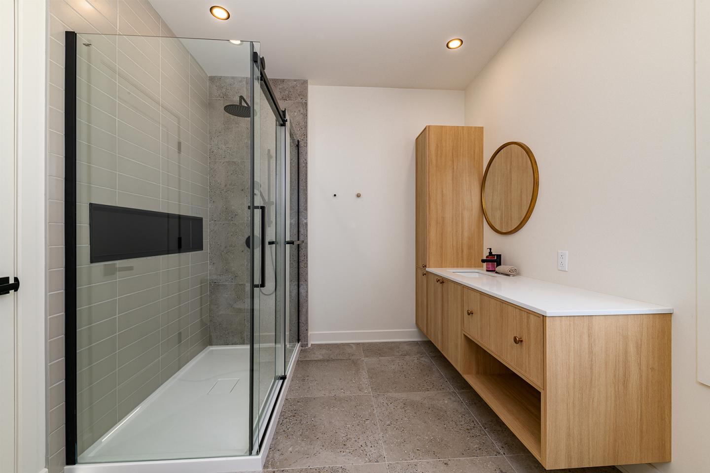 Salle de bain moderne avec douche vitrée et meuble en bois clair.