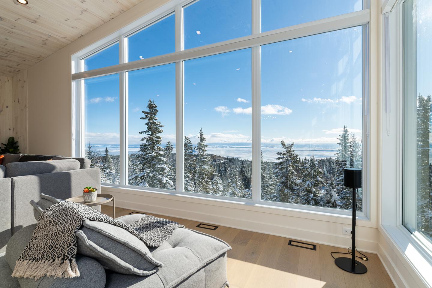 Salon moderne avec vue sur montagne enneigée et ciel bleu par une grande baie vitrée.