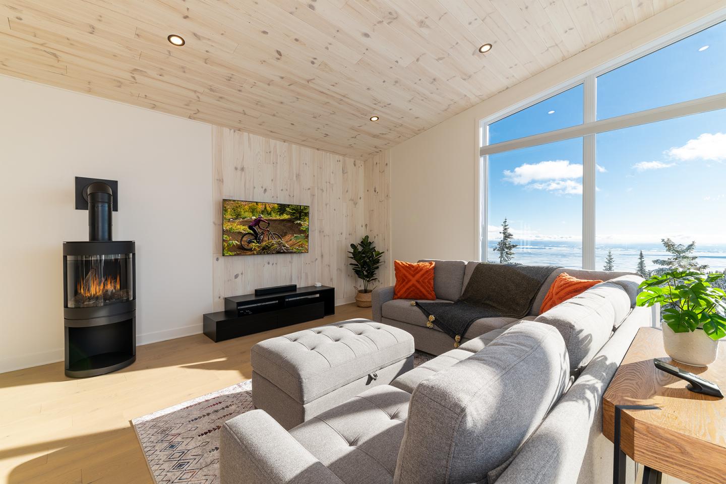 Salon moderne avec canapé gris, poêle noir, grande fenêtre vue sur la mer.