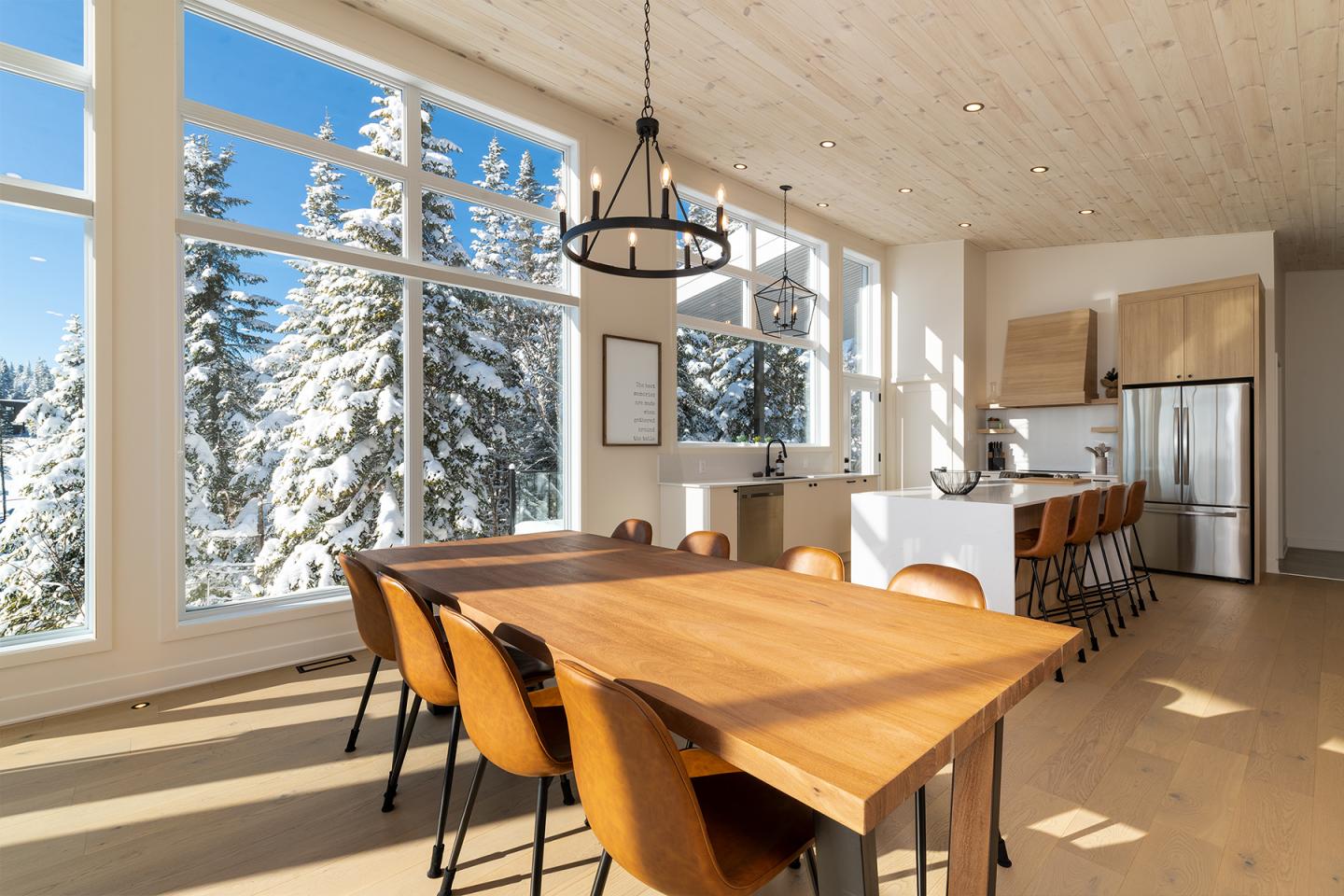 Salle à manger moderne, grandes fenêtres, vue sur forêt enneigée.