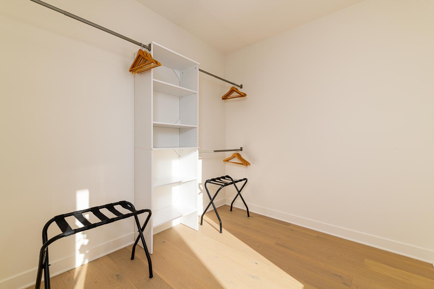 Salle lumineuse avec cintres en bois, étagères blanches et supports à bagages.