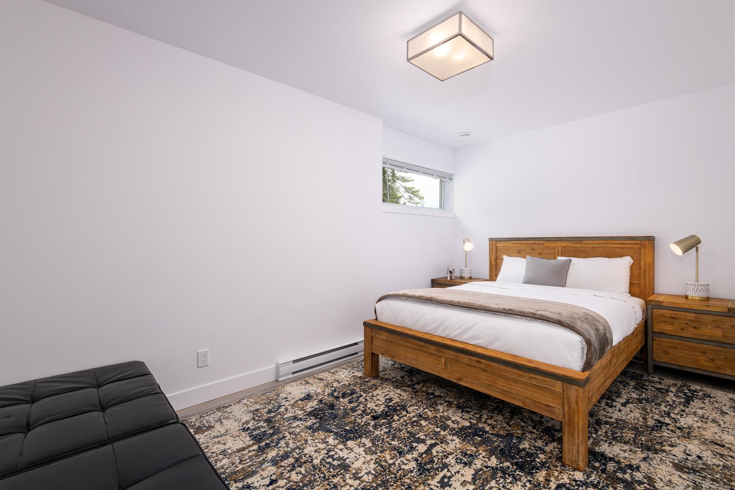 Chambre moderne avec lit en bois, table de chevet et tapis coloré.
