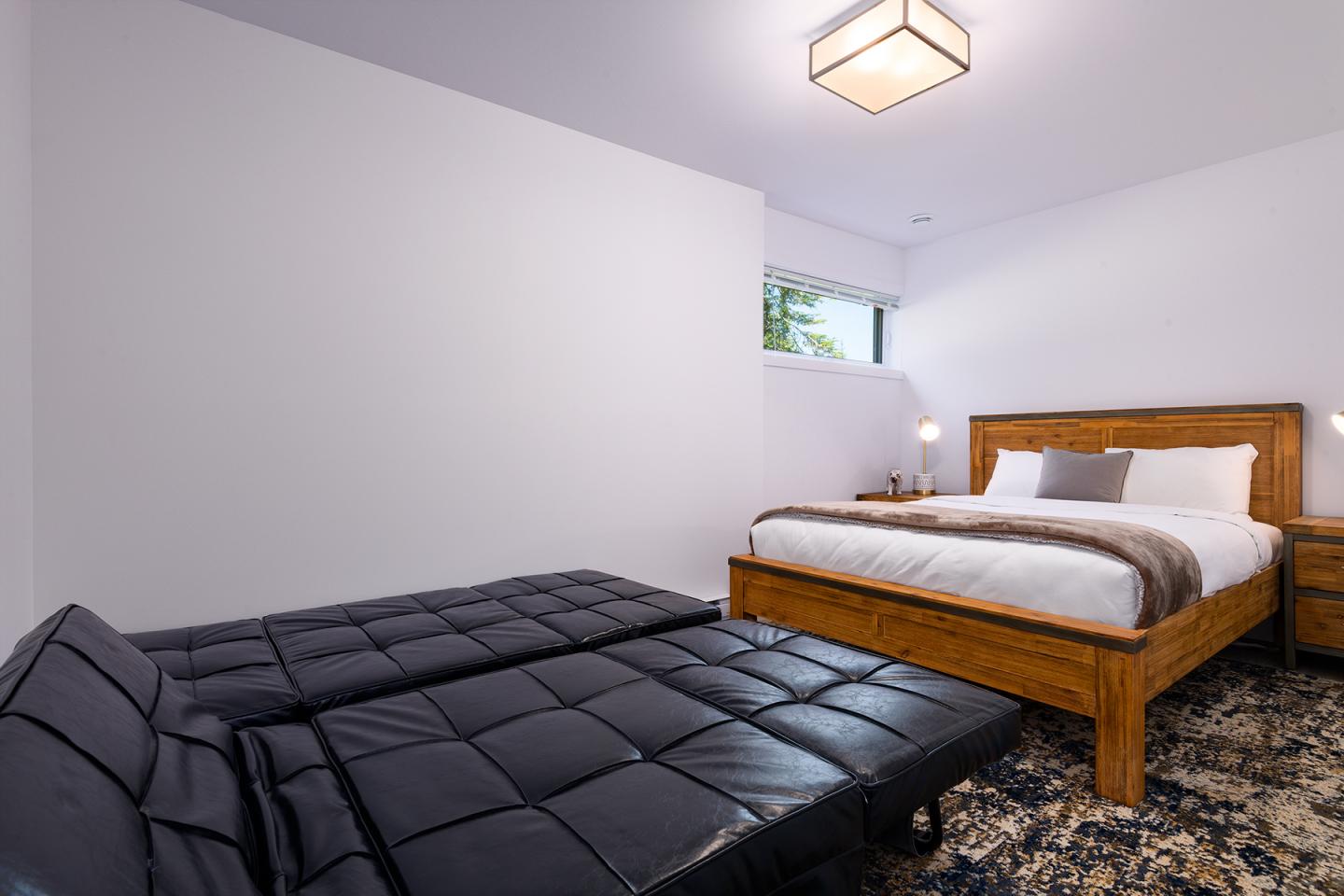 Chambre moderne avec un lit double en bois et un canapé noir convertible.