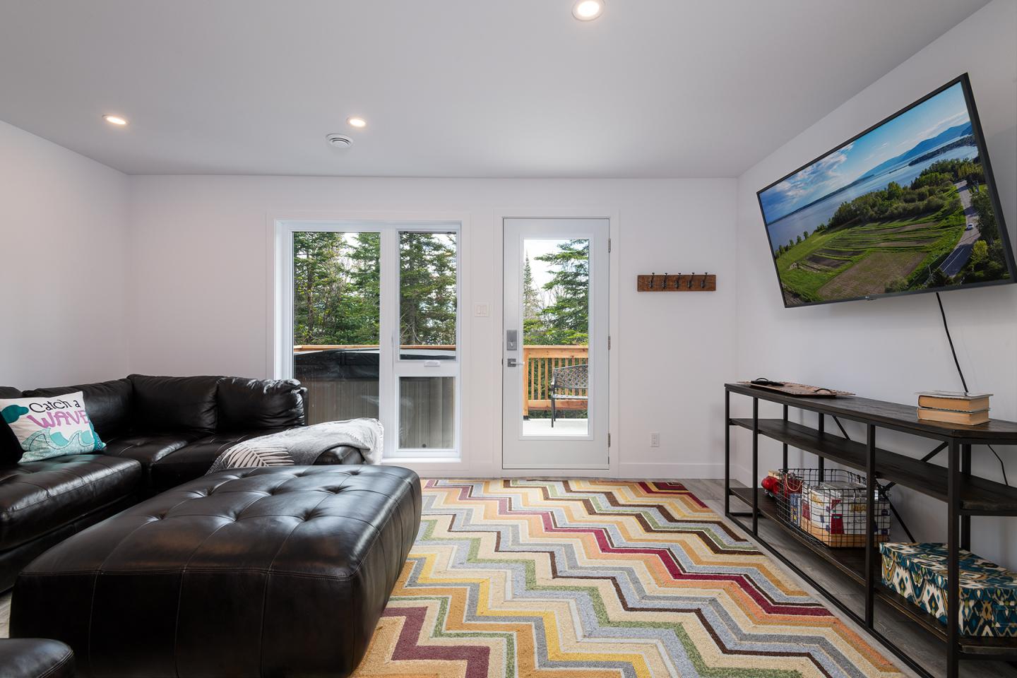 Salon moderne avec canapé noir, TV murale et tapis à motifs colorés.