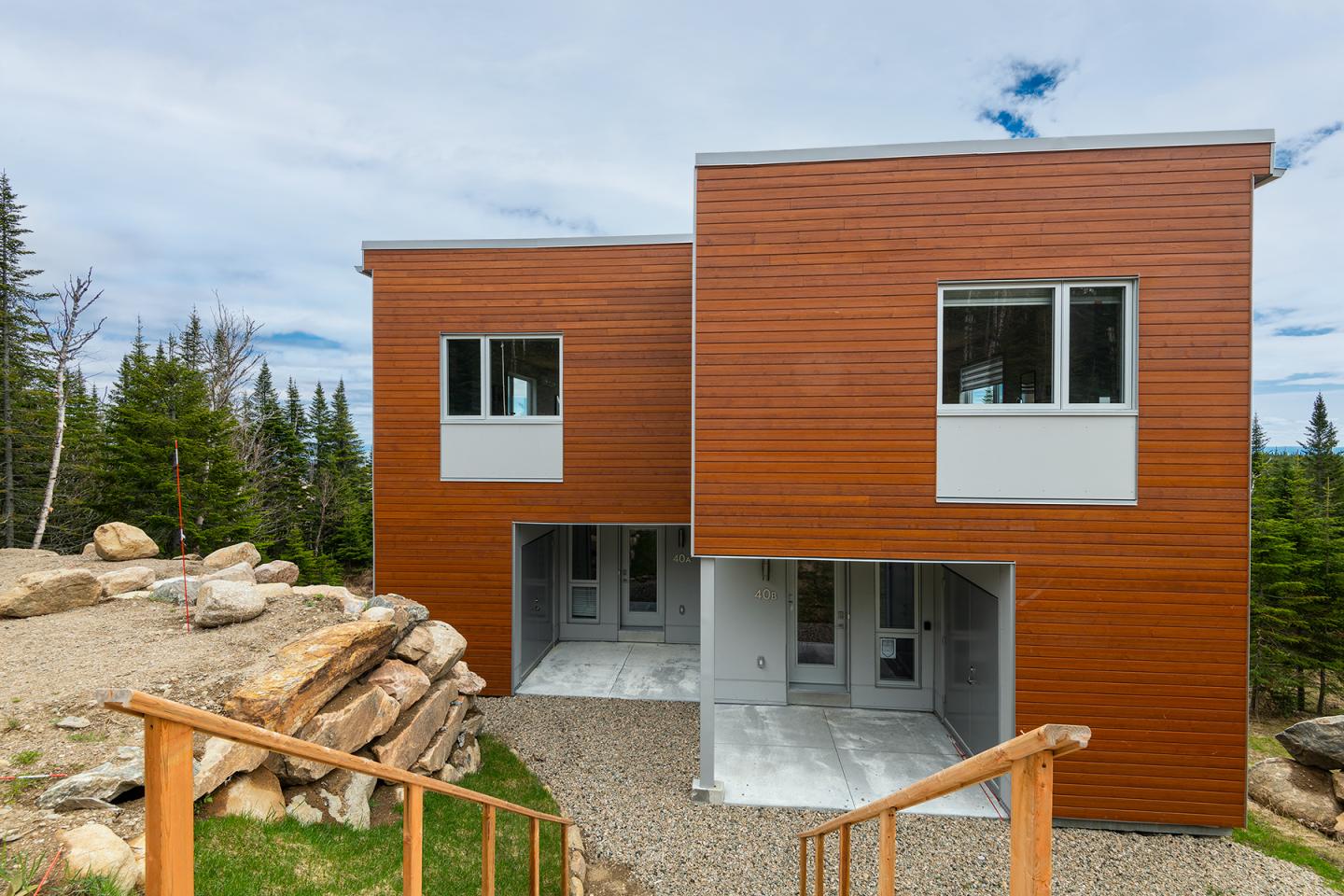 Maison moderne en bois avec grandes fenêtres, entourée d'arbres et de pierres.