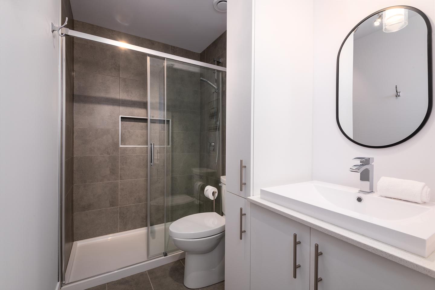 Salle de bain moderne avec douche vitrée et lavabo blanc.