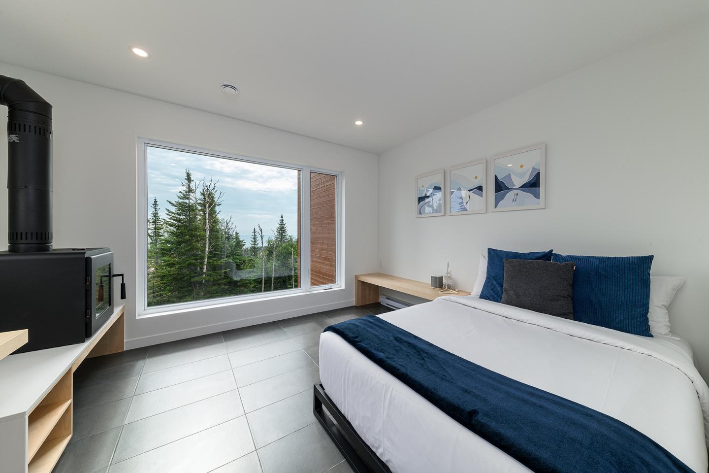 Chambre moderne avec lit, grande fenêtre, vue sur forêt, décoration épurée.