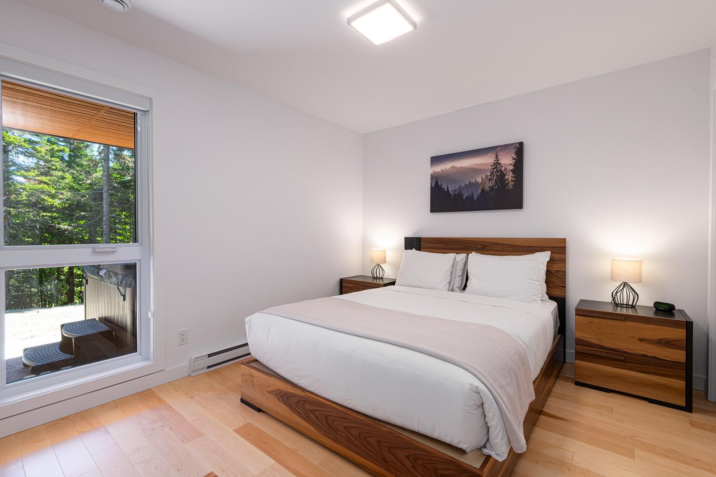 Chambre moderne avec un grand lit et fenêtre avec vue sur la forêt.
