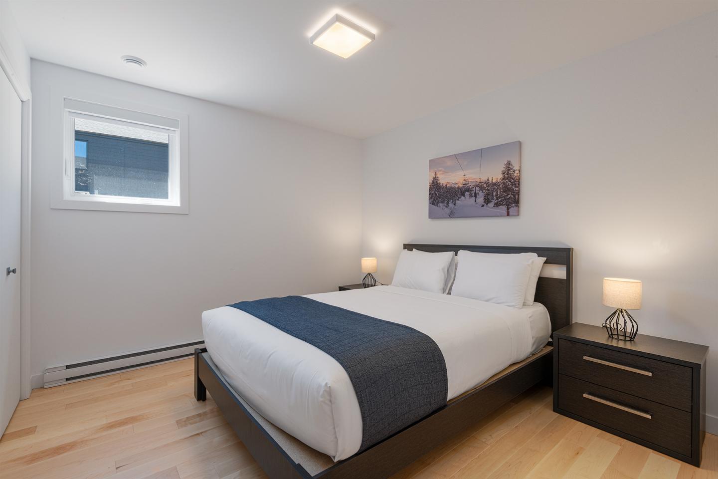 Chambre moderne avec un lit double, deux lampes de chevet et un tableau au mur.