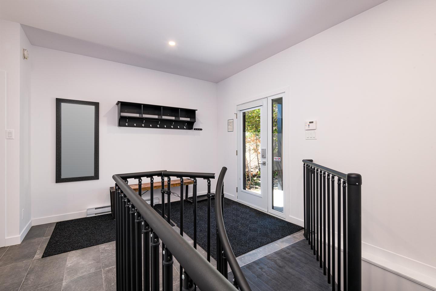 Entrée avec murs blancs, escalier noir et porte-fenêtre donnant sur un jardin.