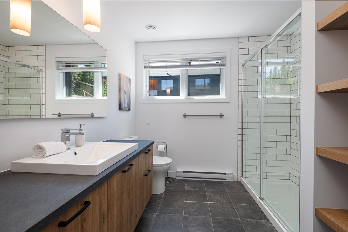 Salle de bain moderne avec lavabo, douche en verre, et carrelage blanc.