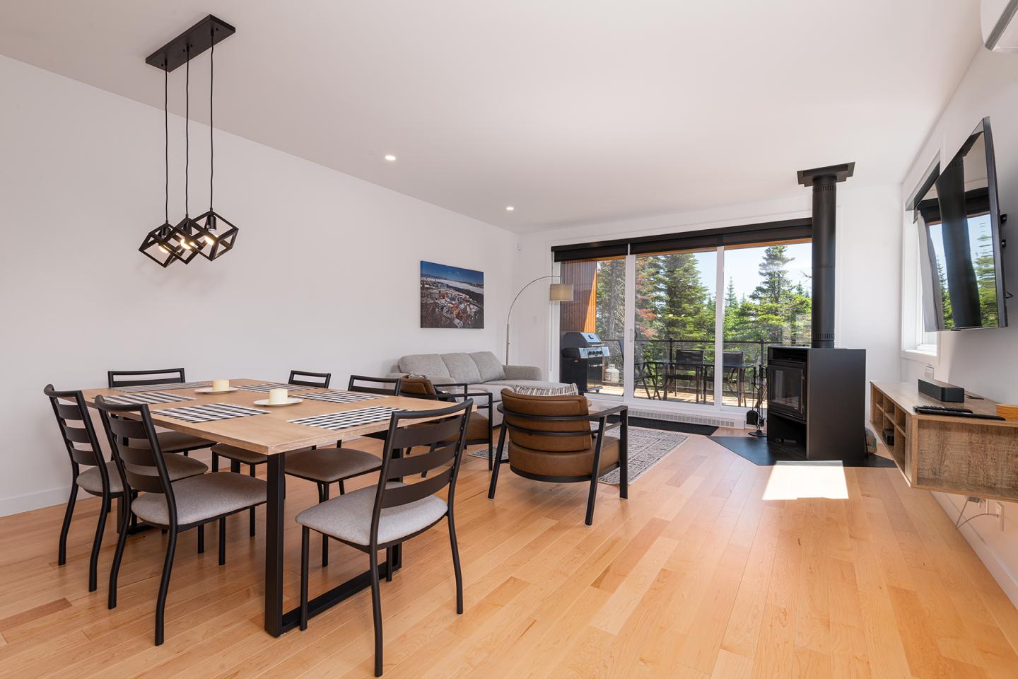 Salle à manger moderne avec table en bois, chaises noires, grandes fenêtres ouvertes sur une terrasse.