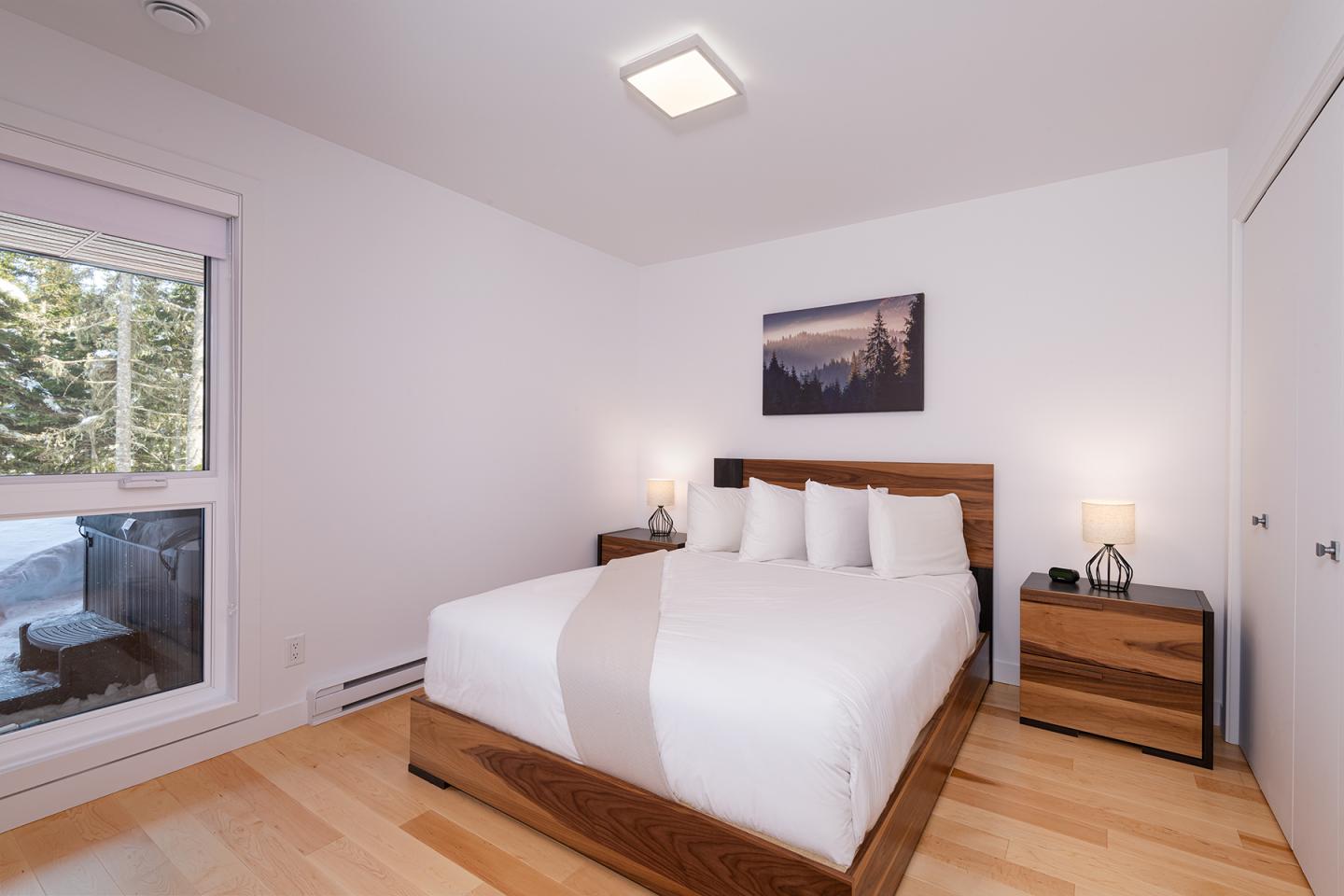 Chambre moderne, lit double, murs blancs, vue sur la forêt par la fenêtre.