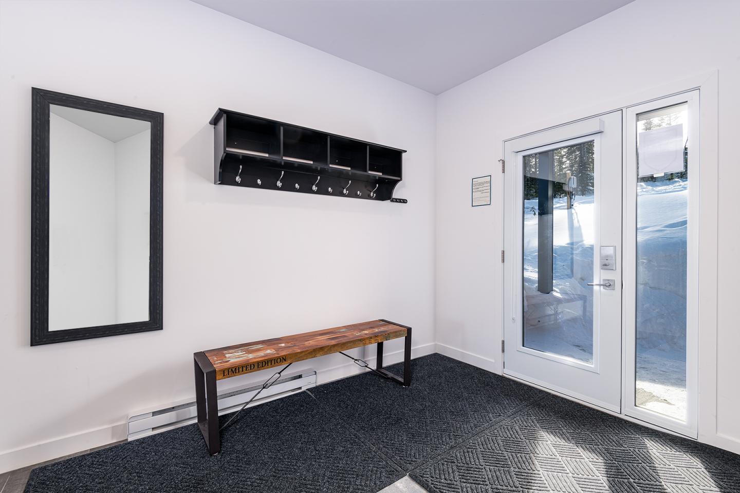 Entrée moderne avec banc, miroir, étagère murale noire et porte vitrée.
