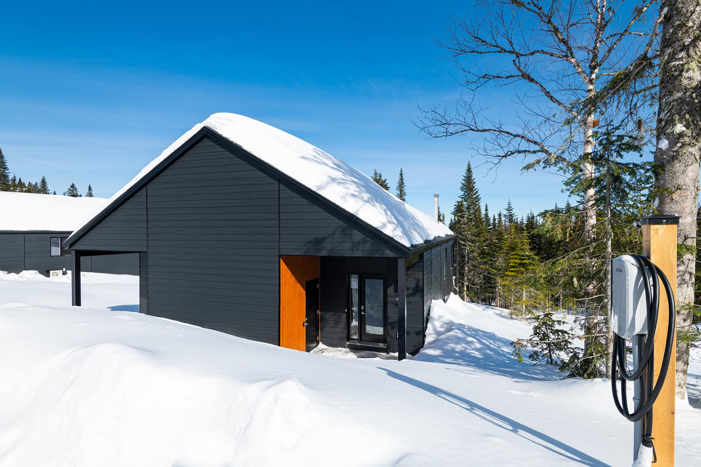 Chalet moderne noir sous la neige, ciel bleu en arrière-plan.
