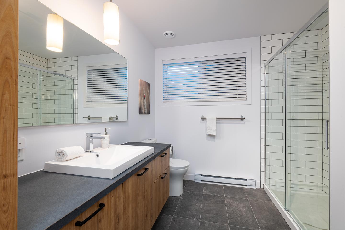 Salle de bain moderne avec douche en verre, lavabo blanc et carreaux blancs.