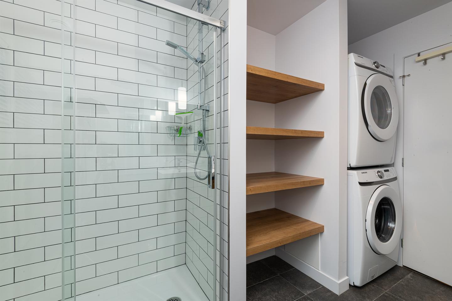Douche moderne, étagères en bois, machines à laver empilées.