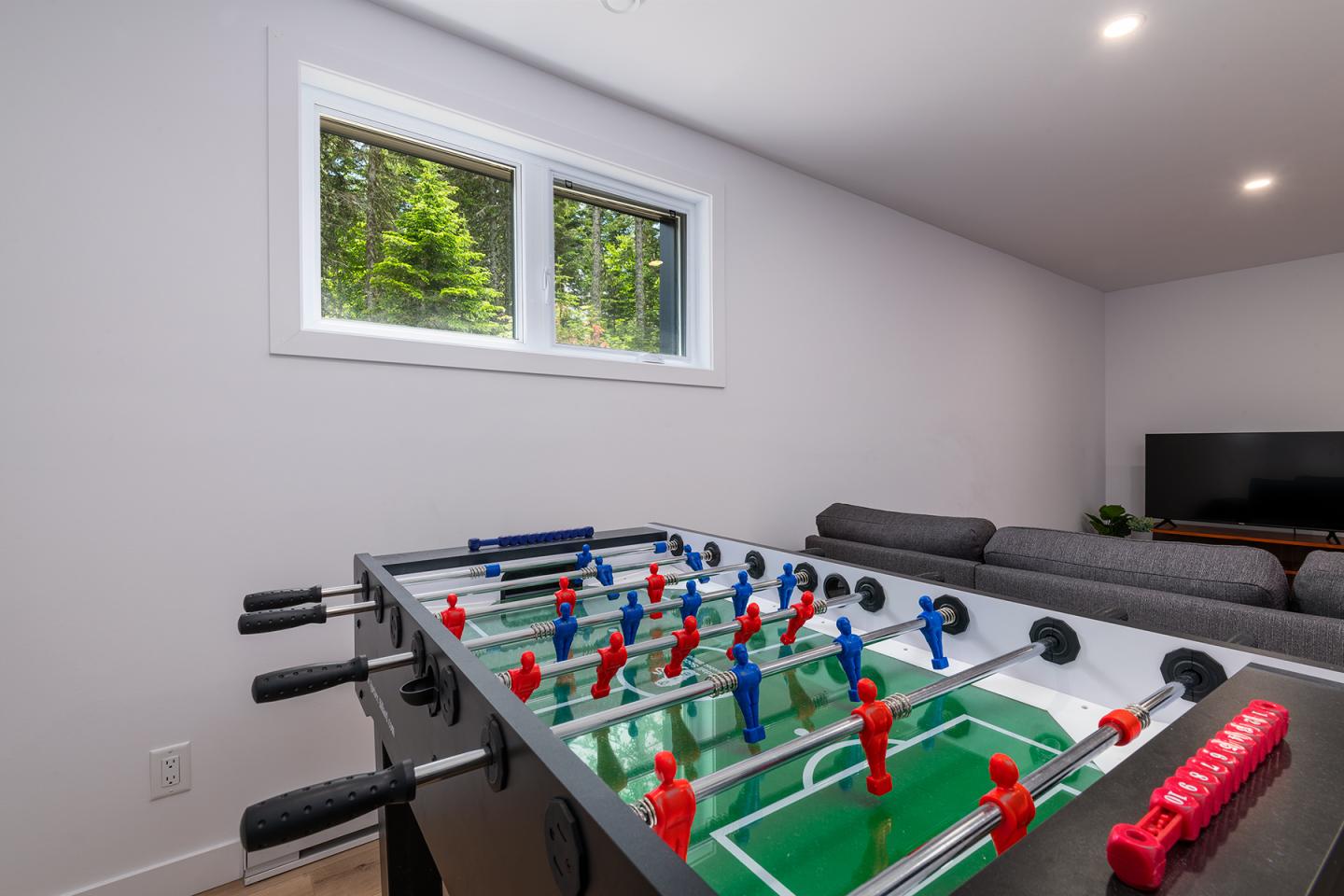 Table de baby-foot dans une pièce lumineuse avec canapé et fenêtre.