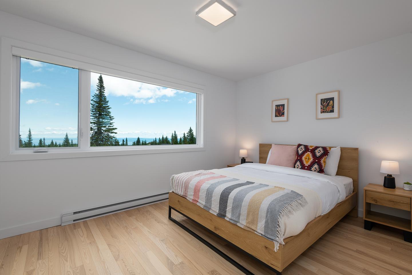 Chambre lumineuse avec lit et grande fenêtre sur paysage boisé.