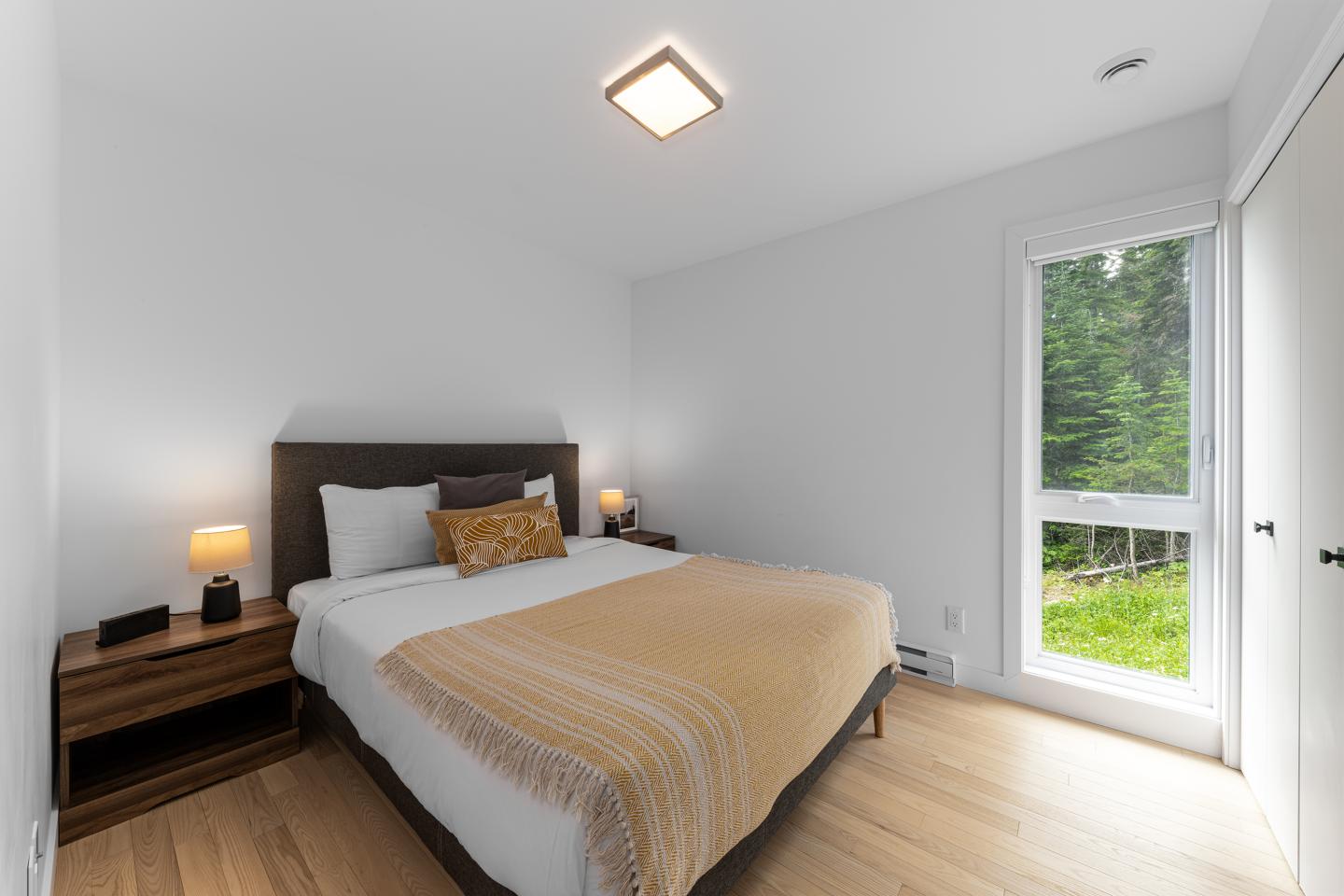 Chambre lumineuse avec lit double, fenêtre ouverte sur jardin verdoyant.