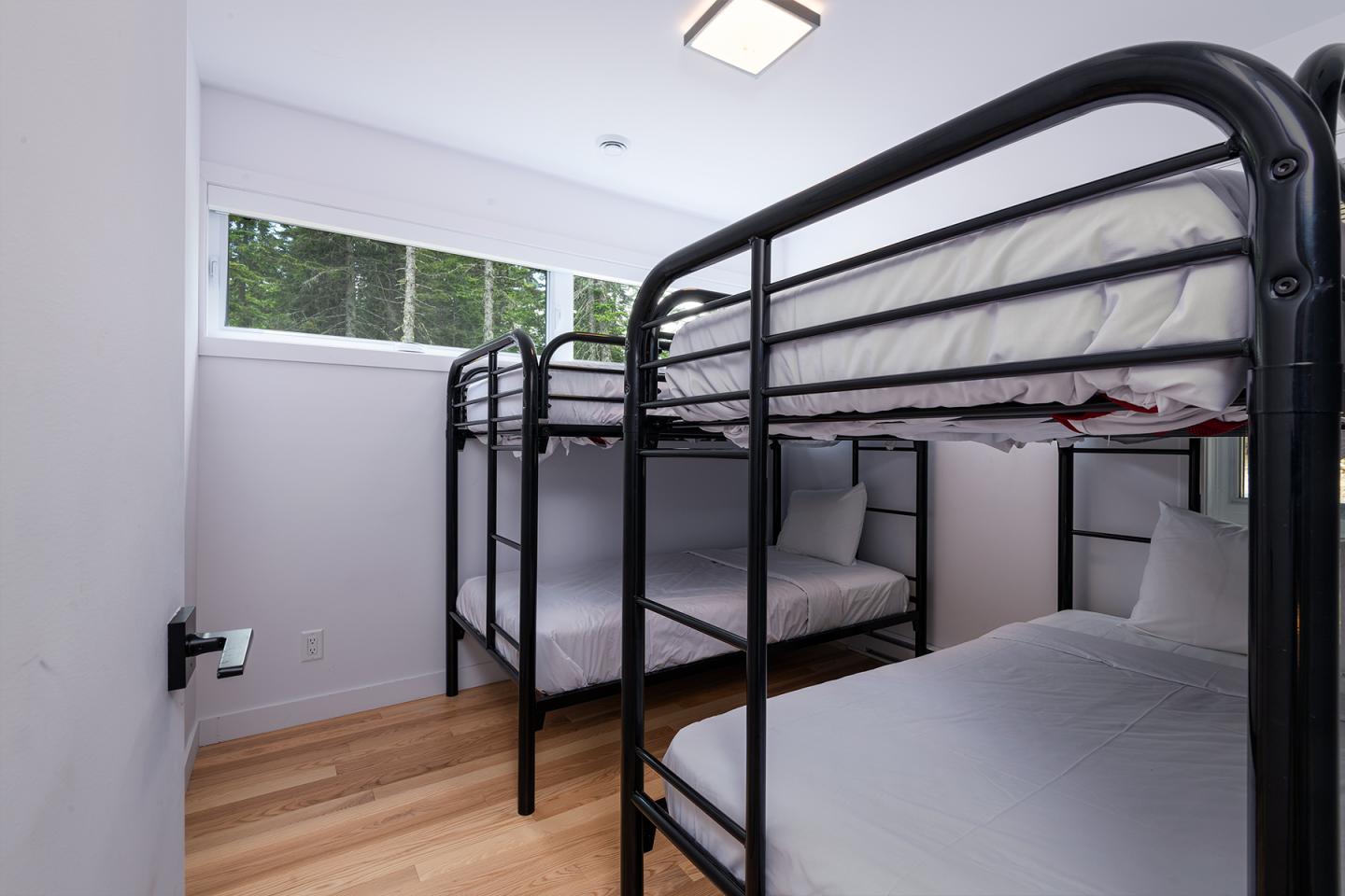 Chambre avec deux lits superposés noirs et fenêtre, plancher en bois clair.