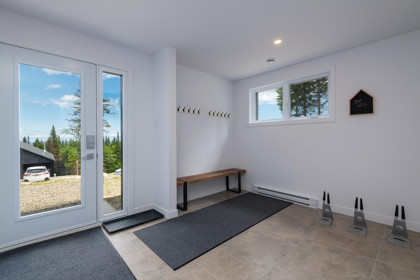 Entrée lumineuse avec porte vitrée, banc et patères, vue sur jardin.