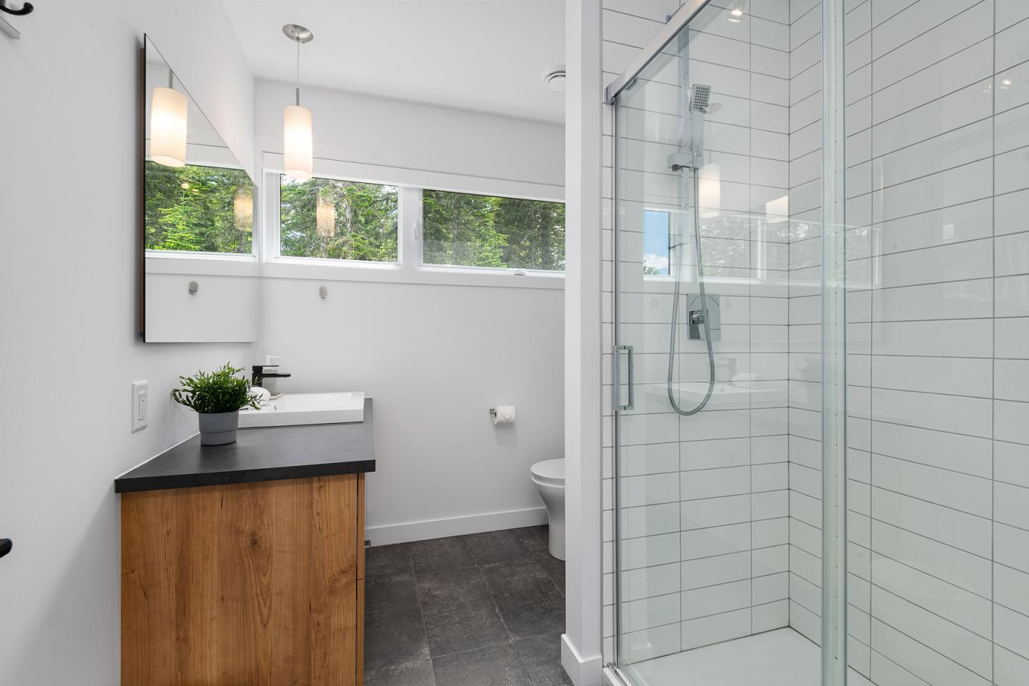 Salle de bain moderne avec douche vitrée, lavabo et meuble en bois.