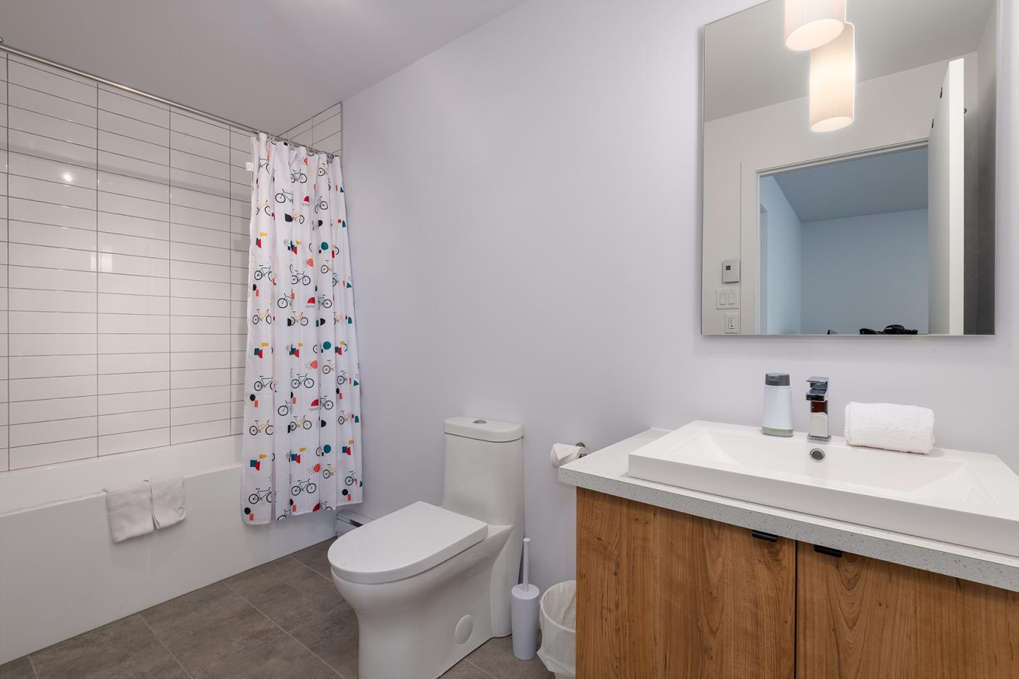 Salle de bain moderne avec baignoire, rideau à motifs, lavabo et miroir.