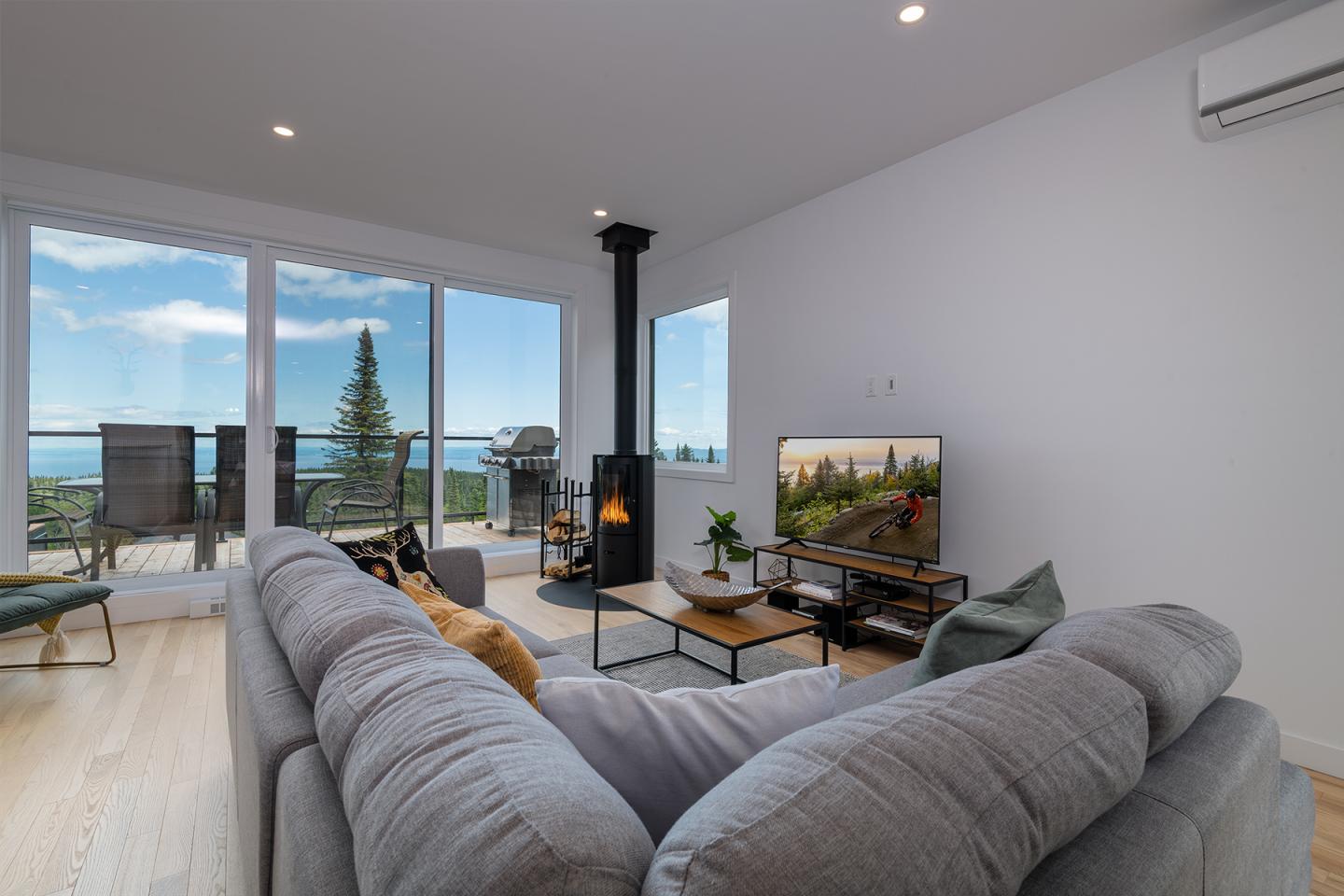 Salon moderne avec canapé gris, cheminée et grande baie vitrée surplombant une vue panoramique.