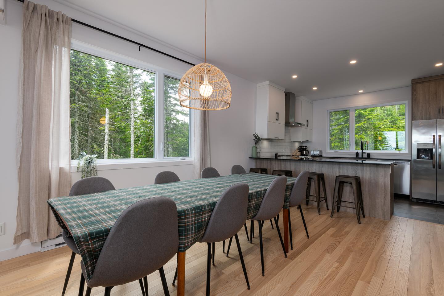 Salle à manger moderne avec table, chaises grises, cuisine équipée en arrière-plan.