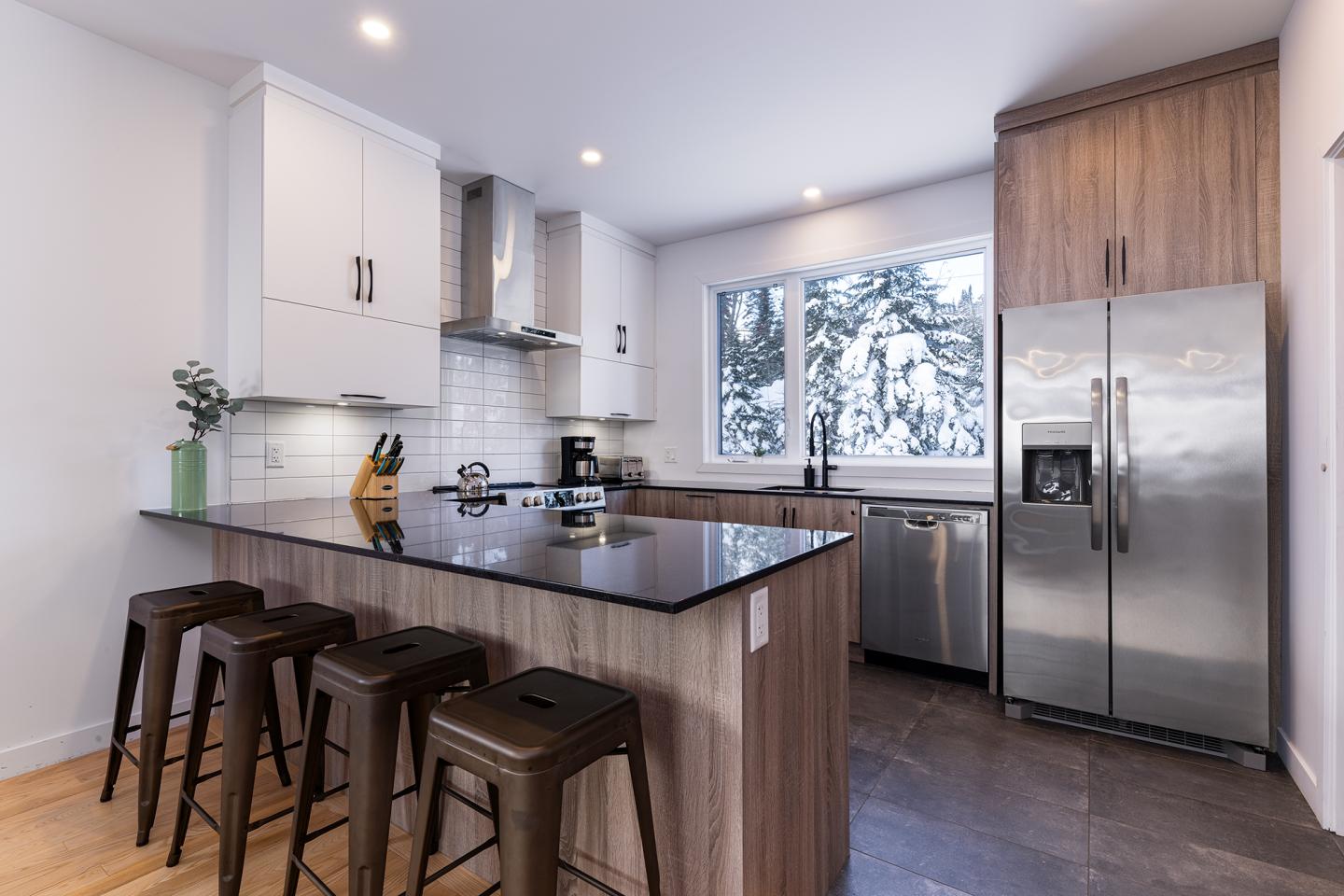 Cuisine moderne avec îlot central, tabourets, et grande fenêtre enneigée.