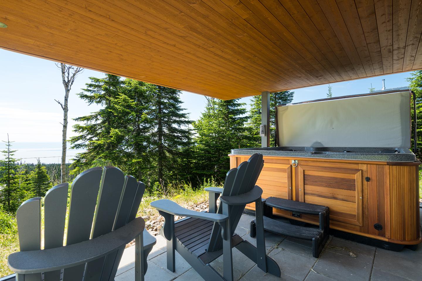 Terrasse avec chaises Adirondack, spa et vue sur les arbres et la mer.