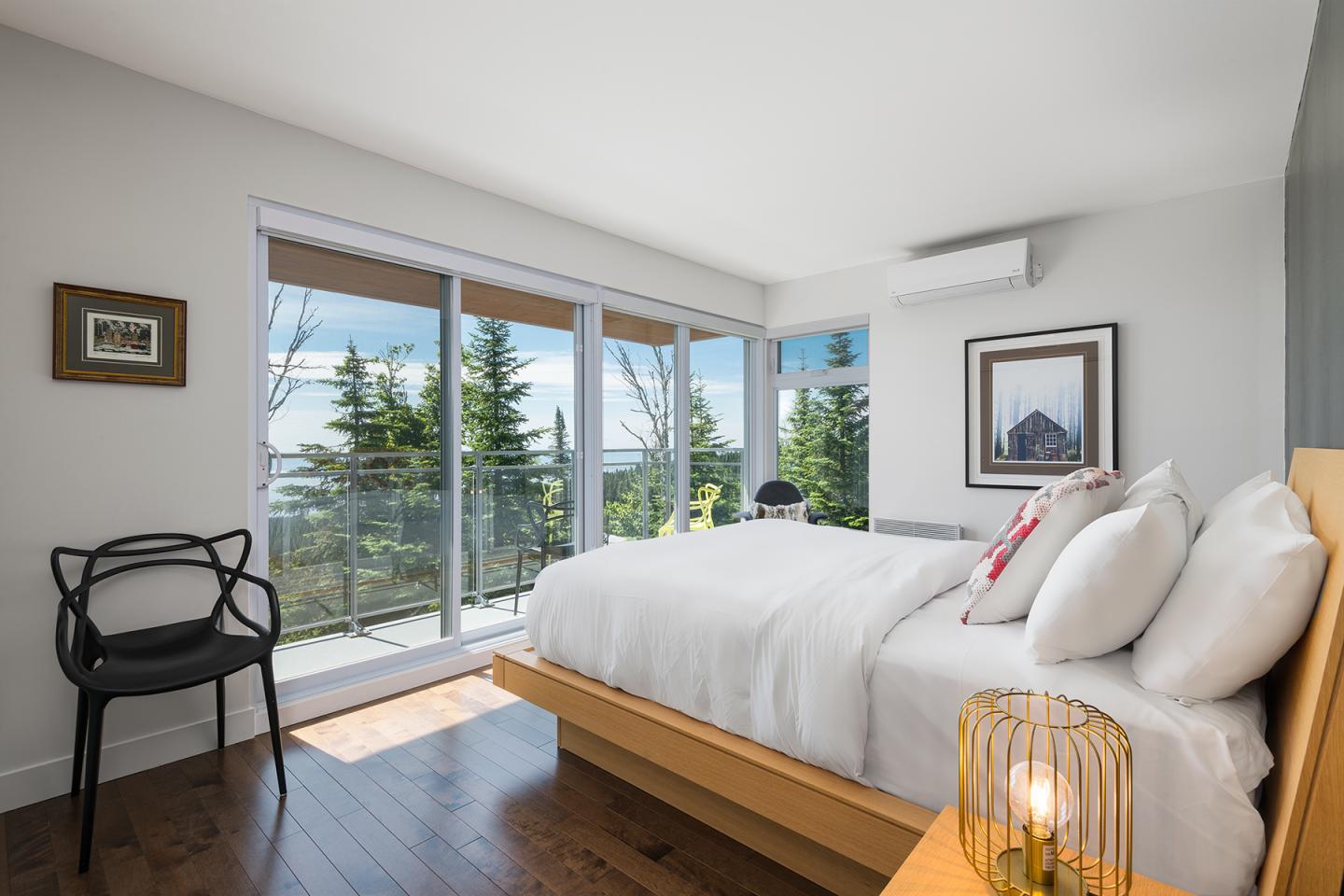 Chambre lumineuse avec lit blanc, fenêtre panoramique, vue sur les arbres.