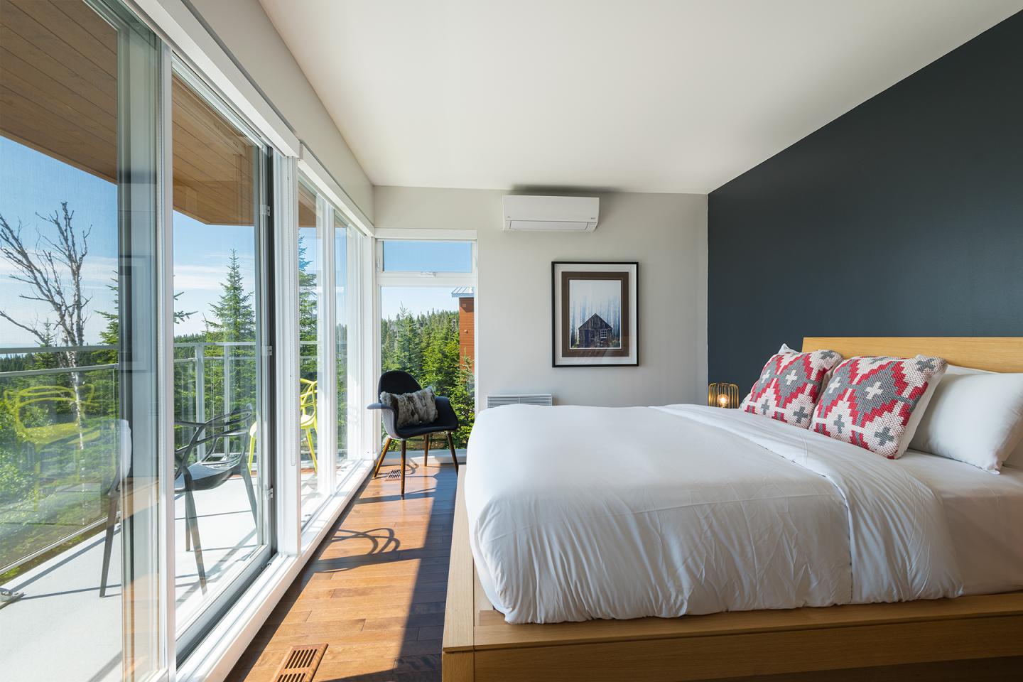 Chambre lumineuse avec grand lit, vue sur balcon et nature.