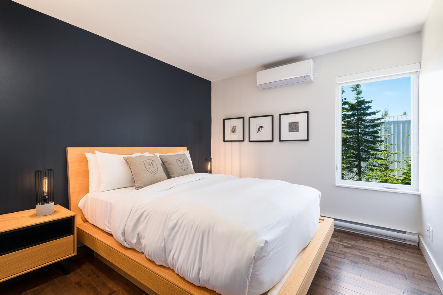 Chambre moderne avec lit double, mur noir et grande fenêtre avec vue sur un arbre.