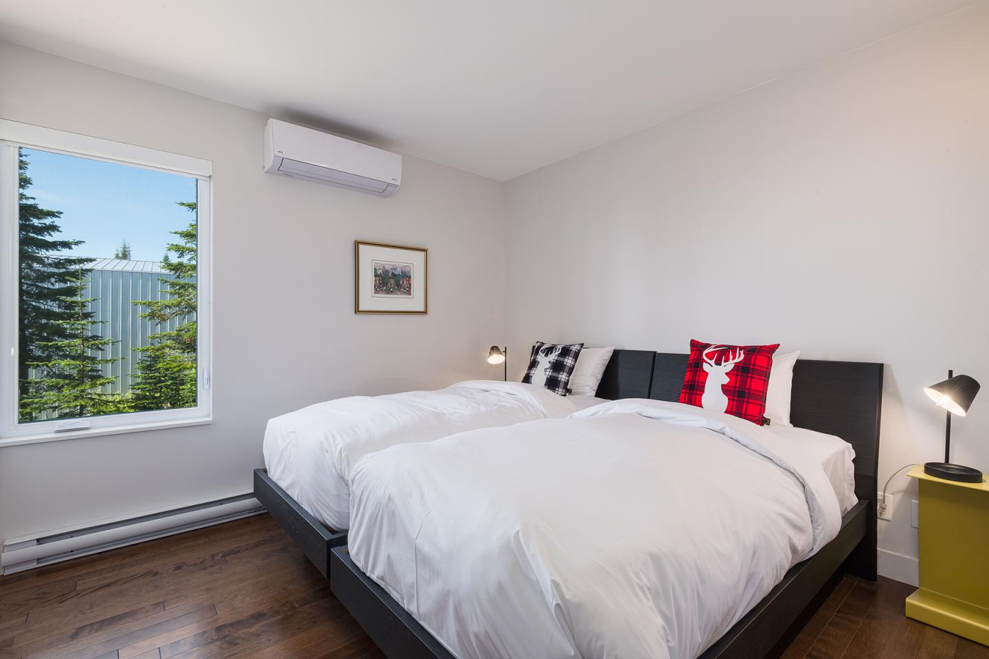 Chambre lumineuse avec deux lits blancs, fenêtre avec vue sur arbres, lampes de chevet.