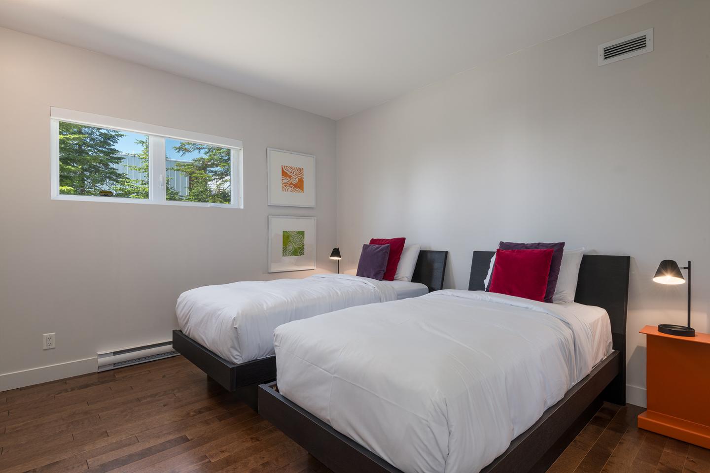Chambre moderne avec deux lits simples, murs blancs et oreillers rouges.