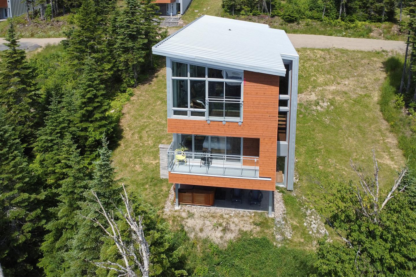 Maison moderne à toit blanc, entourée de verdure.