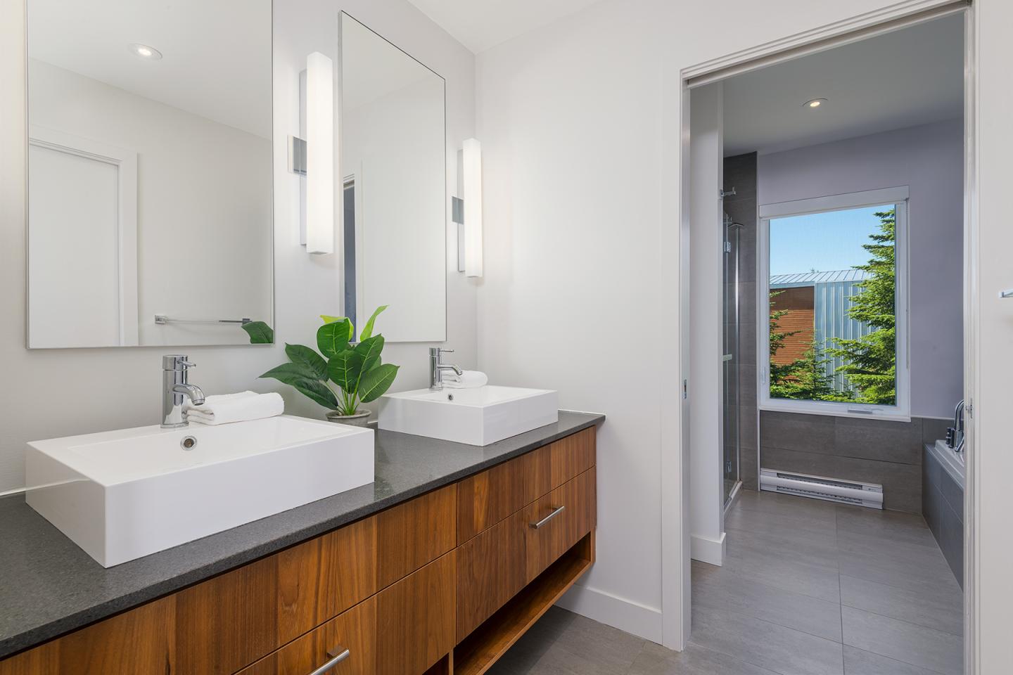 Salle de bain moderne avec deux éviers, miroir et vue sur jardin.