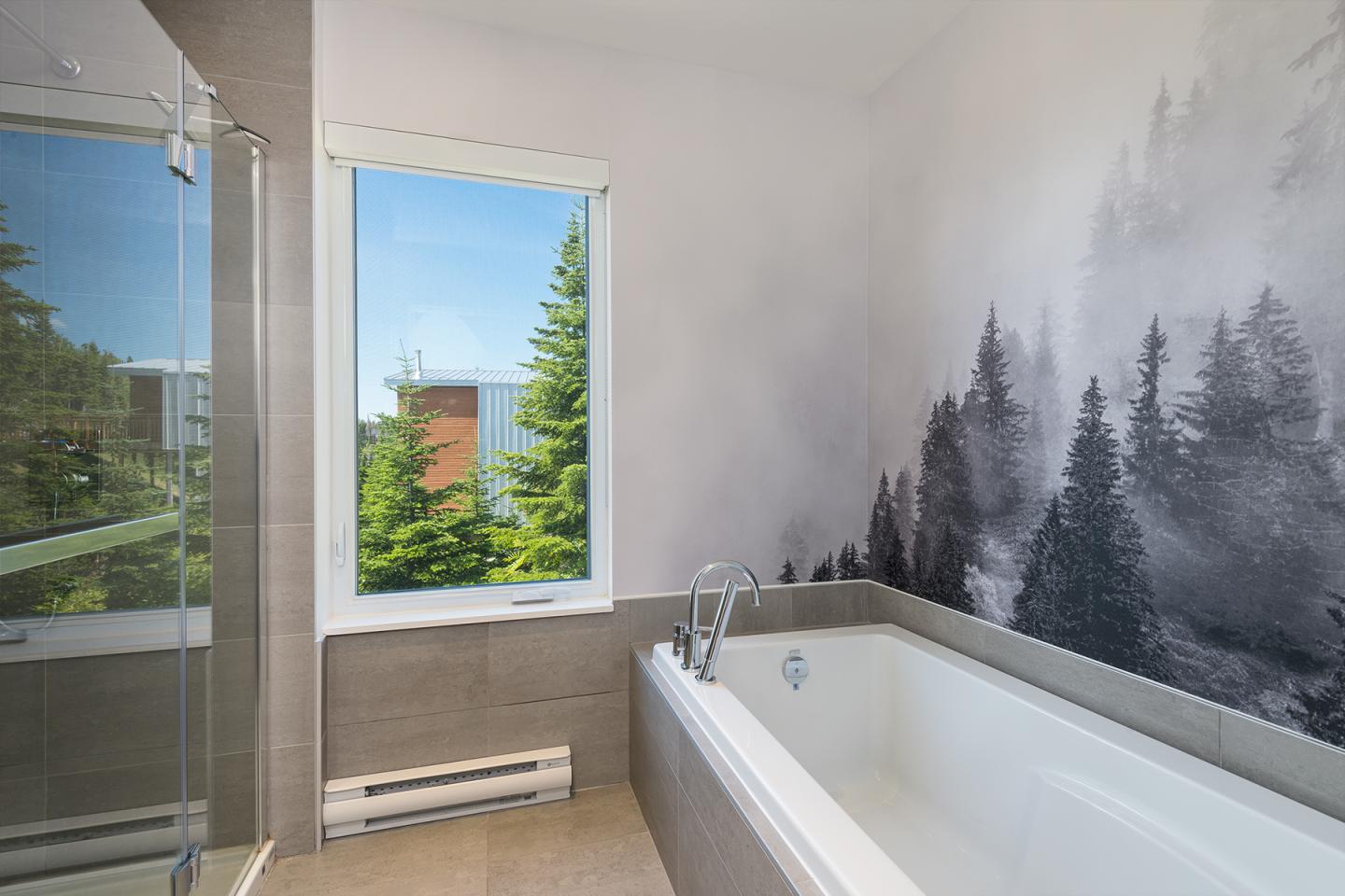 Salle de bain moderne avec baignoire, fenêtre et mur décoré de motifs d'arbres.