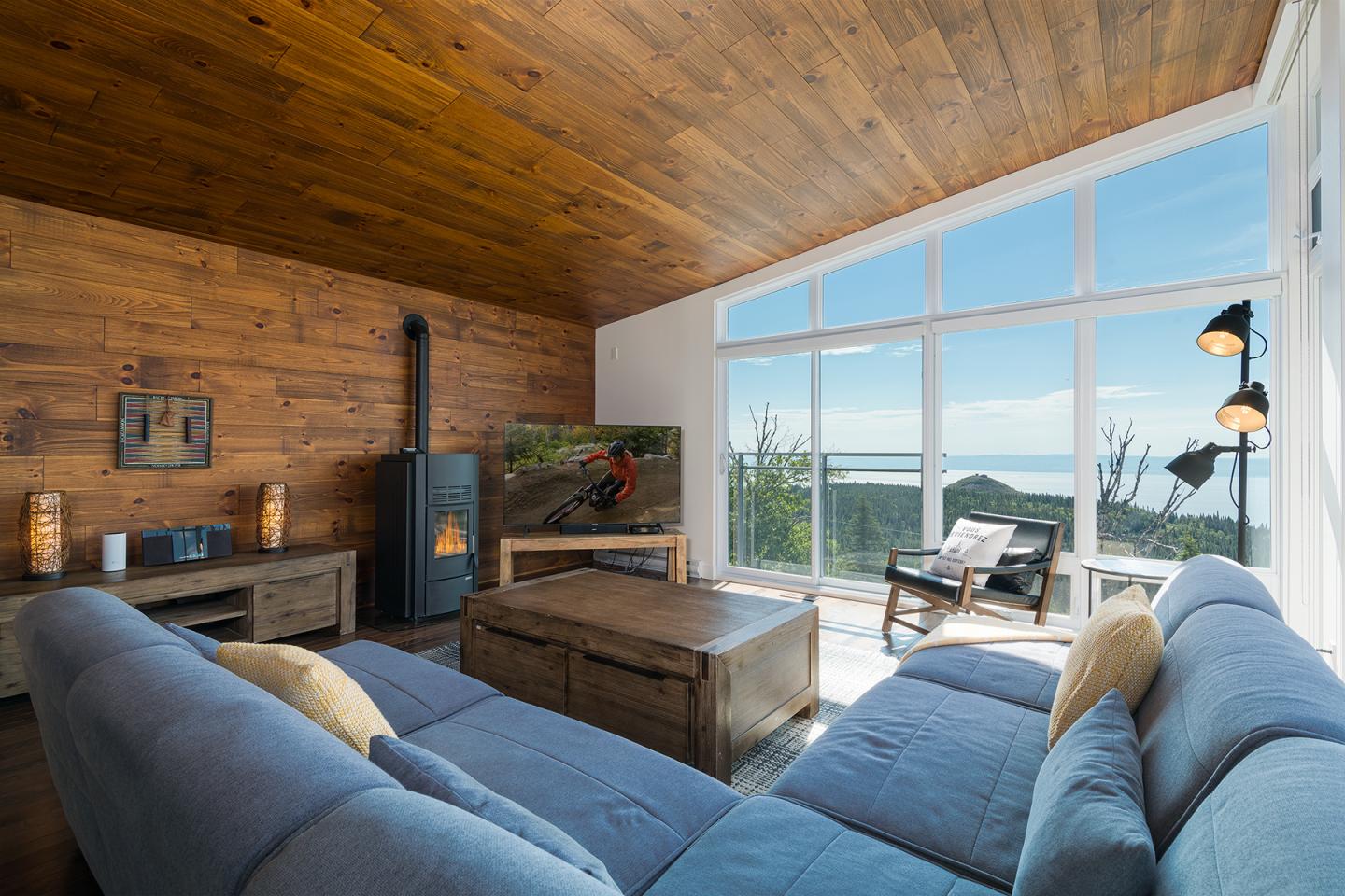 Salon lumineux avec canapé bleu, grande fenêtre et vue sur la mer.