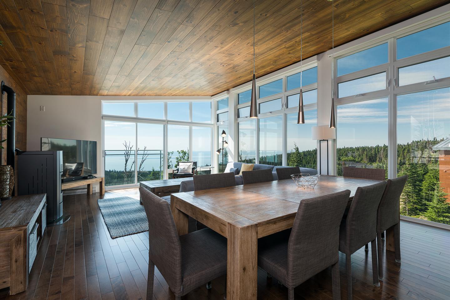Salle à manger moderne avec vue panoramique sur la mer et forêt, table en bois.