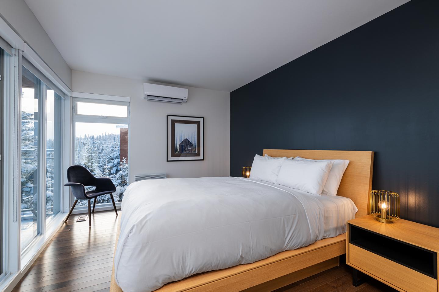 Chambre moderne avec lit double, mur sombre, grande fenêtre et fauteuil noir.