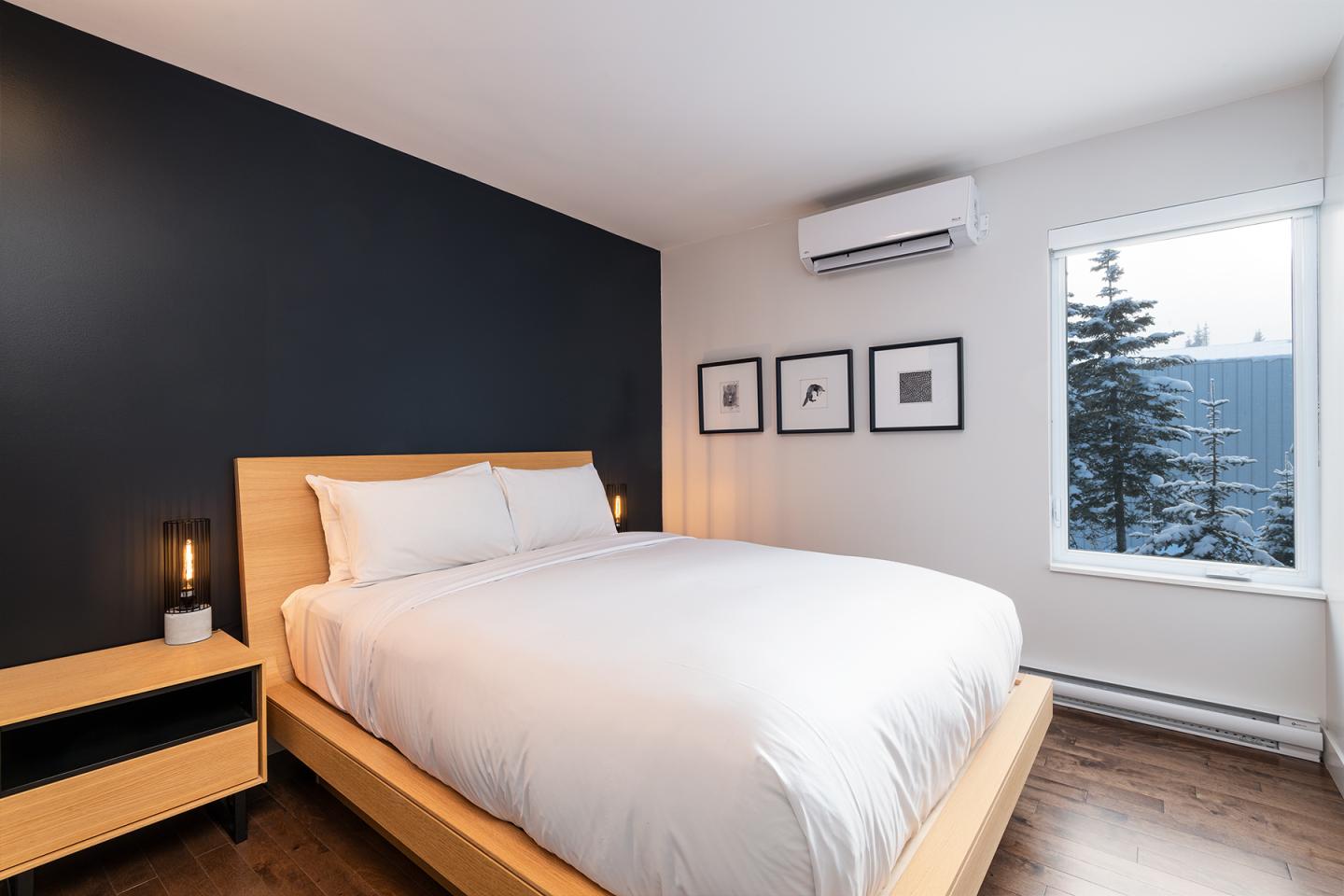 Chambre moderne avec lit double, murs noirs et blancs, et fenêtre avec vue sur un arbre.