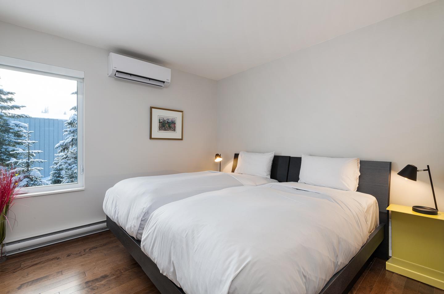 Chambre lumineuse avec lit double, lampes de chevet et fenêtre avec vue sur arbres enneigés.