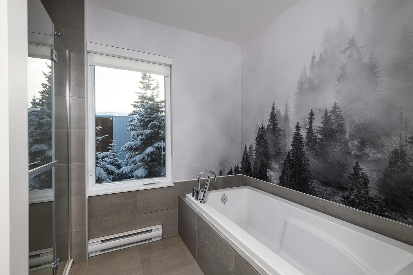 Baignoire moderne avec vue sur arbres enneigés et mur forêt en noir et blanc.